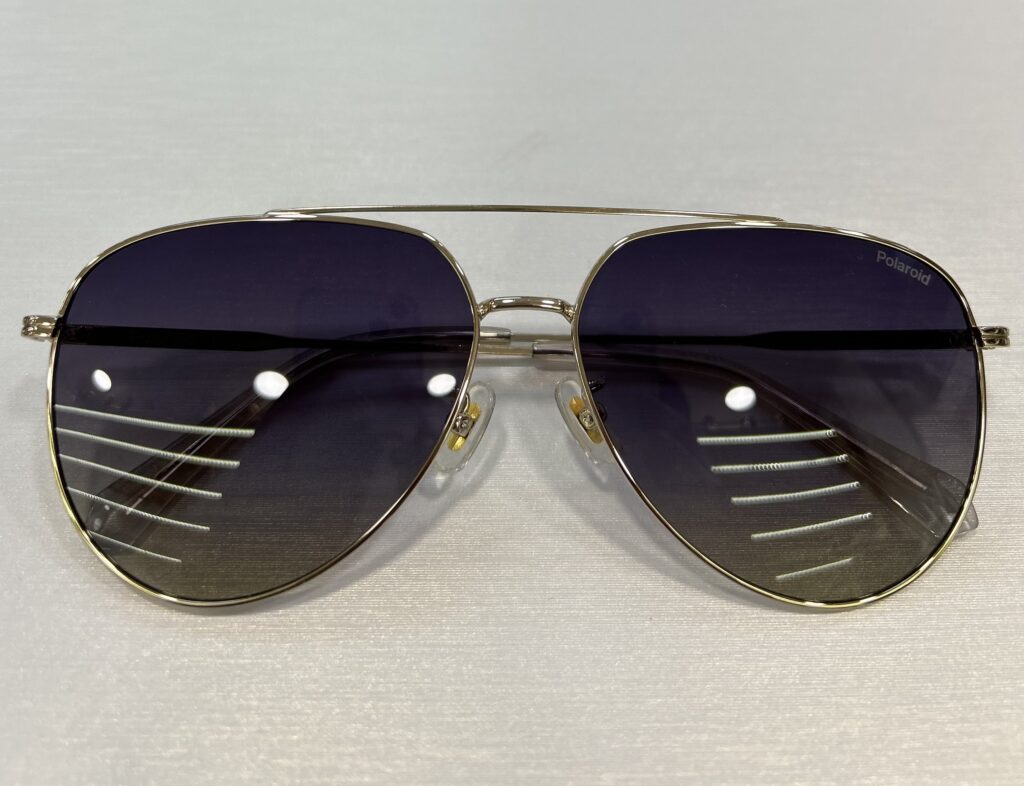 A pair of aviator-style 眼鏡 with dark tinted lenses and a thin metal frame is placed on a flat surface. The brand "Polaroid" is visible on one lens.