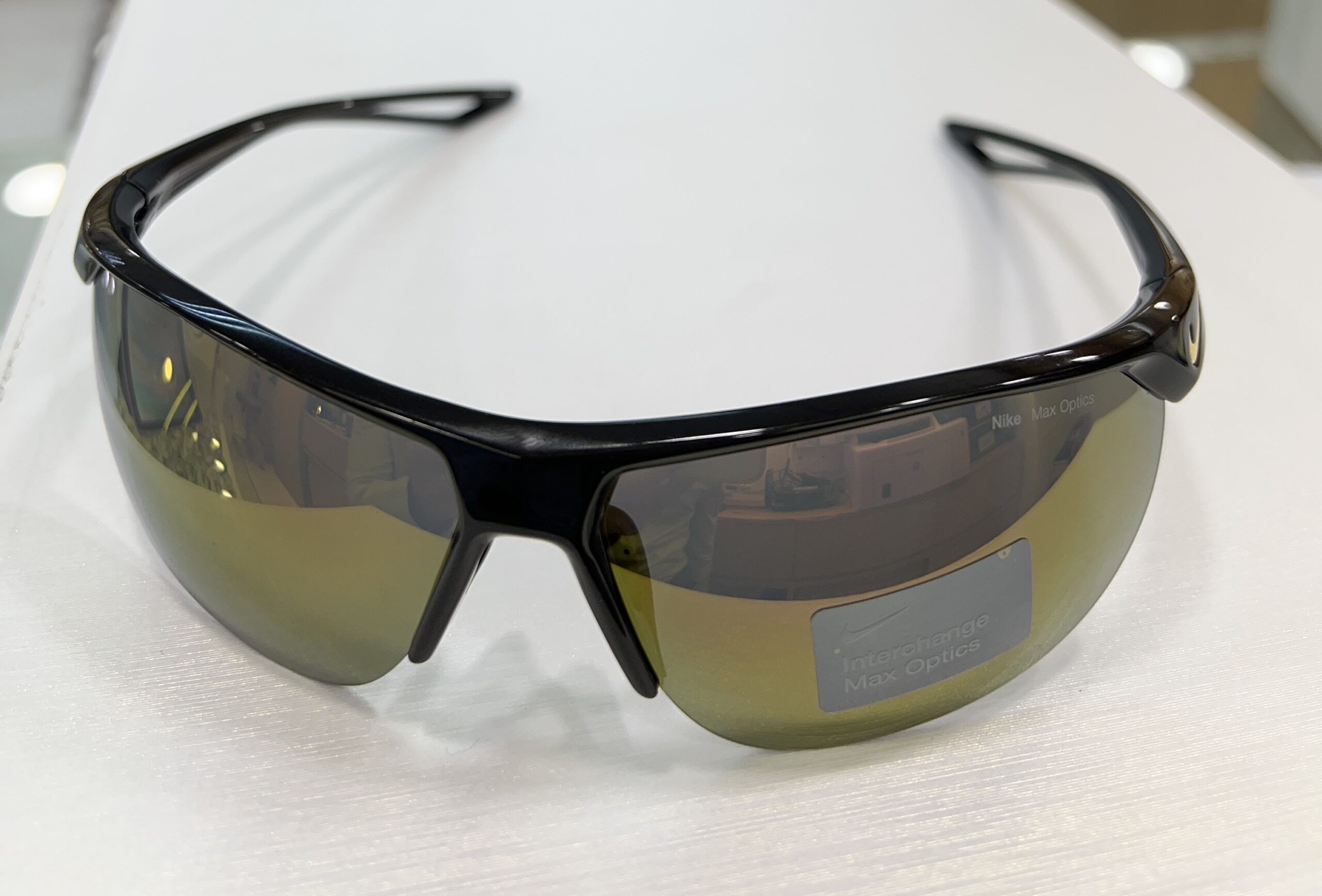 A pair of black sports sunglasses with yellow-tinted auto draft reflective lenses resting on a white surface.